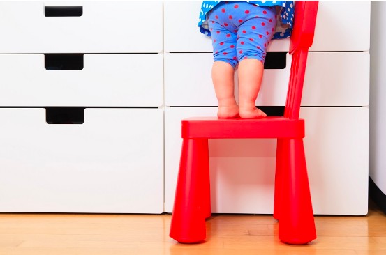 Acidentes domésticos: saiba quais são os ambientes mais perigosos da casa; imagem mostra as pernas de uma criança pequena em cima de uma cadeira vermelha em frente a um armário branco
