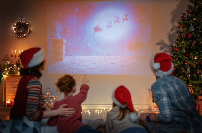 Família com gorros de Natal assiste a projeção de filme na parede da casa