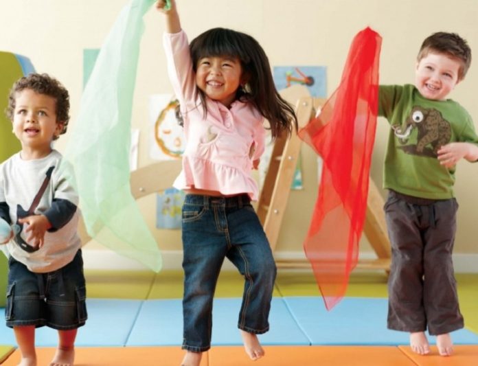 Sugestões de brincadeiras como a da imagem em que três crianças estão em pé em movimento, saltanod, com braço estendido