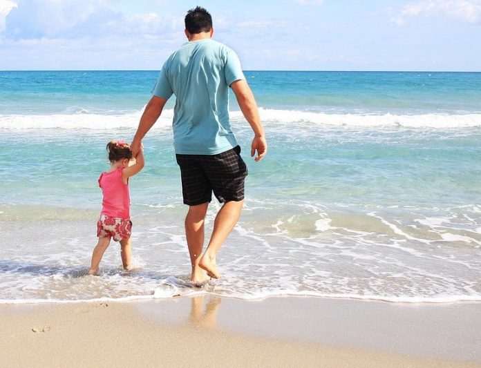 Pai e filha caminham de mãos dadas na praia, primeira infância