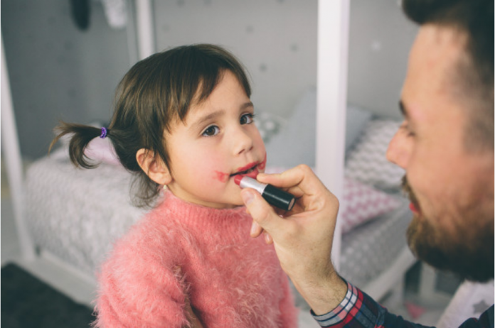 Maquiagem em crianças é permitida, desde que sem exageros; pai passa batom na boca de menina