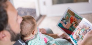 Pai e bebê olham para livro infantil ilustrando matéria sobre programa 'Conta Pra Mim', do MEC, que incentiva leitura na primeira infância.