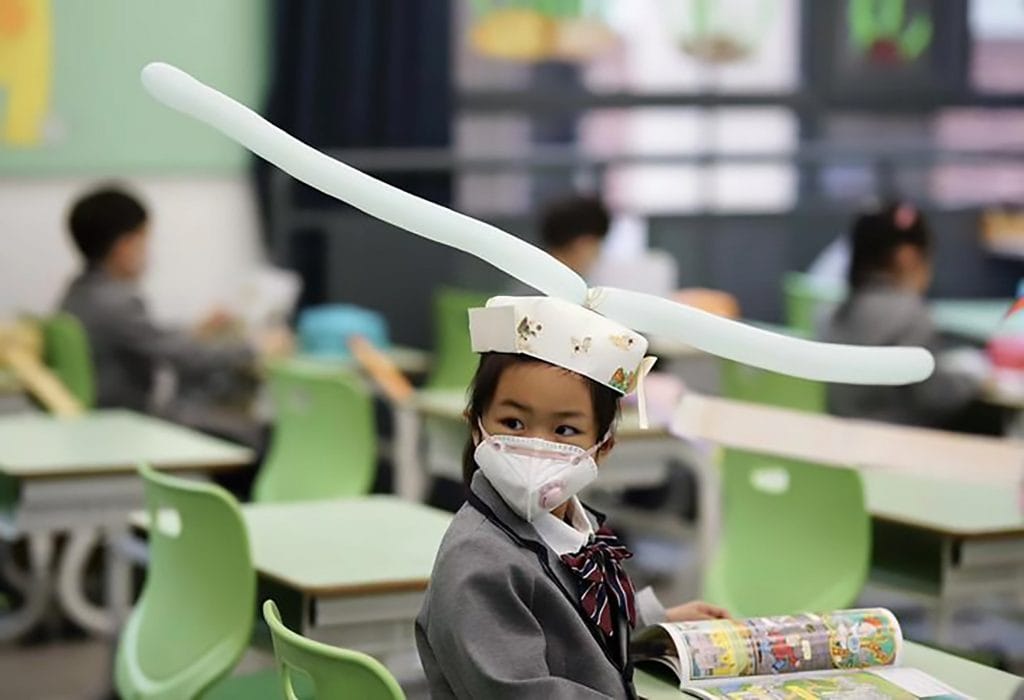 Crianças chinesas usam chapéus na escola para manter distanciamento social e evitar propagação do coronavírus. 
