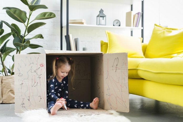 Criança brinca dentro de caixa de papelão toda rabiscada. Criar um lugar em casa que a criança possa ir para se acalmar é uma das dicas da Disciplina Positiva que ajudam na autorregulação e no autocontrole.