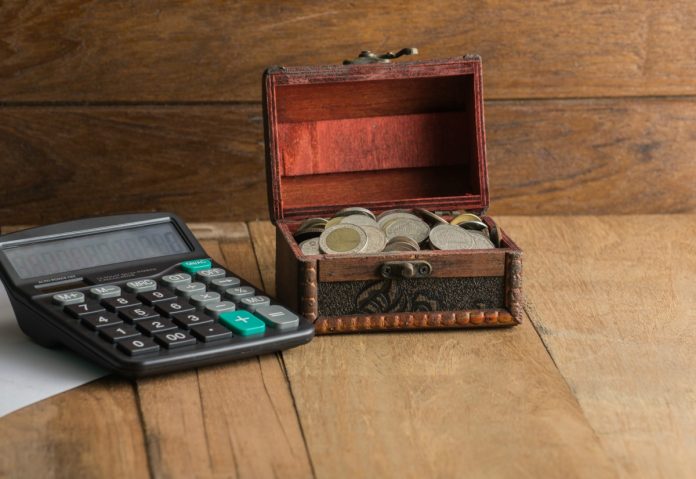 Uma calculadora e um pequeno baú antigo com moedas remetem à importância dos pais aproveitarem materiais antigos da casa para criar cofrinhos com as crianças e ensinar a elas educação financeira
