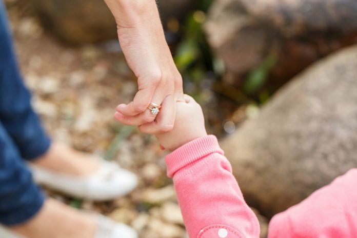 Imagem mostra a mão de uma mãe segurando no bracinho de uma bebê de blusa rosa. Apesar do grande número de crianças disponíveis para adoção, a maioria delas (83%) tem mais que dez anos, idade pouco aceita pelos pretendentes a pais