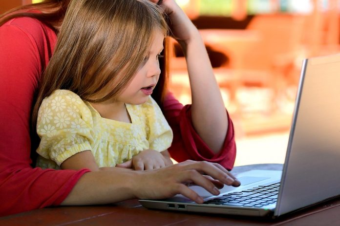 Menina e mãe sentam juntas em frente a um notebook, ilustrando matéria sobre preocupações dos pais em relação às crianças na internet.