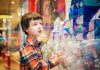 Criança está parada em frente à vitrine de loja que parece ser de brinquedos, ilustrando matéria relacionada a publicidade infantil.