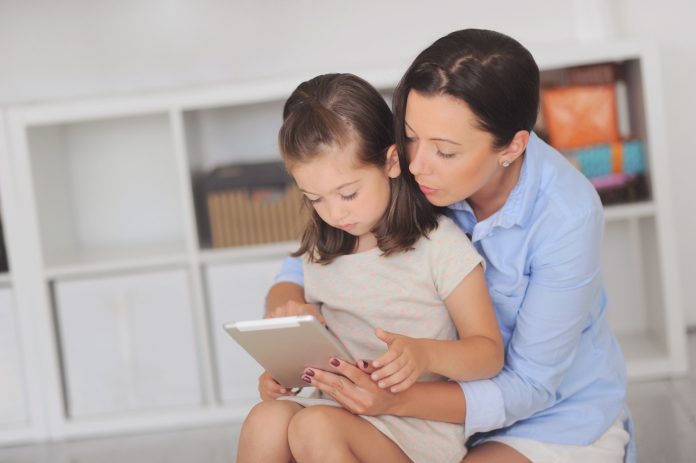 Mãe e filha leem livro digital em tablet, ilustrando matéria sobre como conversar sobre pandemia com crianças.