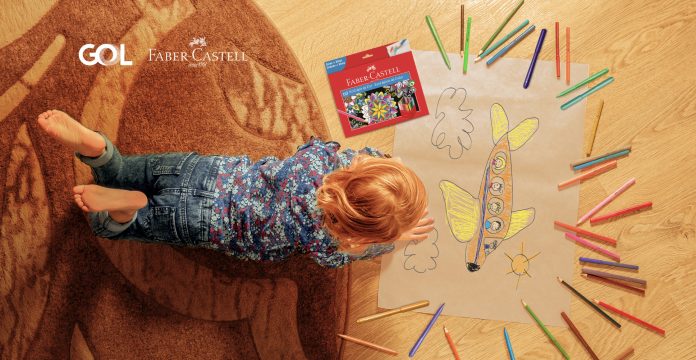 Criança deitada no chão desenha avião usando lápis de cor da Faber-Castell, em ilustração à matéria sobre o projeto Colorindo o Dia.