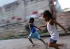 Escolas de concreto, que poderiam ser como essa imagem – em que duas crianças negras correm em um piso de cimento com uma parede ao fundo acimentada também – não incentivam o brincar e o cuidar