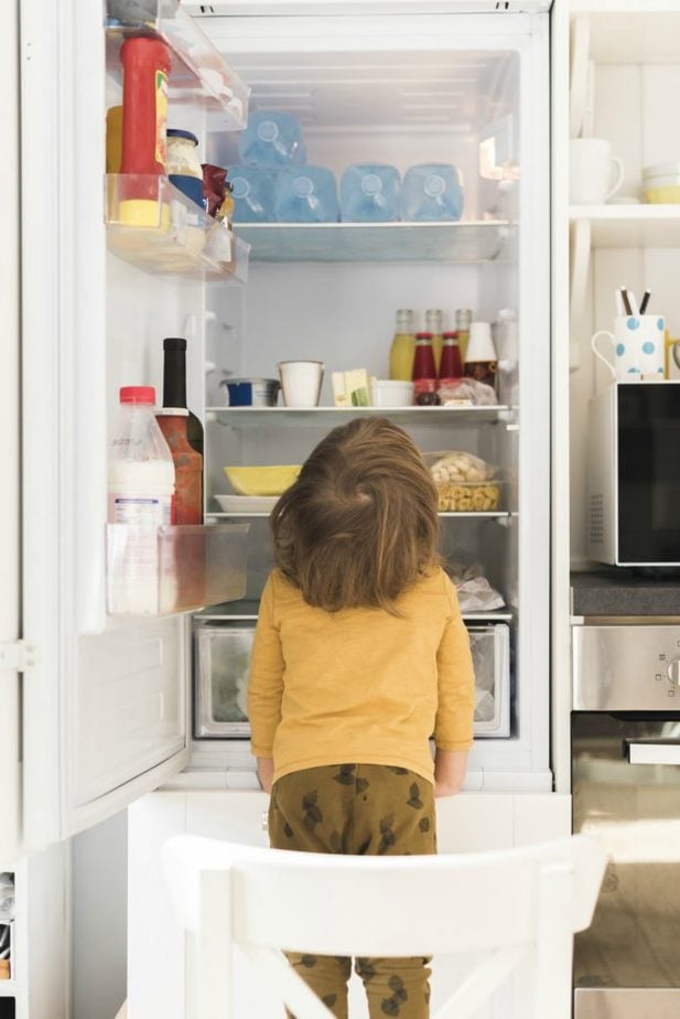 Se seu filho está comendo demais, como esse garoto da imagem que está em cima de um banco com a geladeira aberta escolhendo algo para comer, veja atitudes para ajudá-lo e assim evitar que ele engorde nesta pandemia