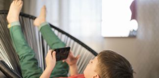 Tempo dedicado às telas, como o garoto desta imagem que assiste algo pelo celular deitado em uma cadeira, é alvo de mais um alerta da Sociedade Brasileira de Pediatria