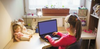 Perda auditiva na infância pode ser provocada por causas como volume alto no fone de ouvido, como essa garota da imagem que usa o fone de ouvido e olha para o computador