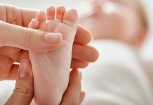 Mão de adulto toca em pezinho de bebê