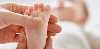 Mão de adulto toca em pezinho de bebê