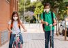 Reabertura de escolas privadas: Fenep mostra previsões de retorno em todo o país; imagem remete a dois alunos, uma menina que anda na bicicleta e um menino que anda de patinete, ambos com mochila nas costas a máscara