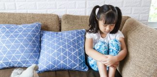 Criança triste na quarentena, como essa gaorta asiática de cabeça baixa no sofá: saiba o que os pais podem fazer para ajudar os filhos