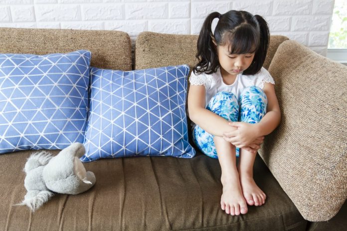 Criança triste na quarentena, como essa gaorta asiática de cabeça baixa no sofá: saiba o que os pais podem fazer para ajudar os filhos