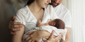 Pai e mãe estão abraçados e seguram um bebê no colo; Obstáculos para tornar a licença-maternidade mais longa no Brasil
