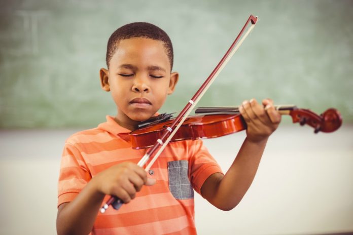 Estimular o talento das crianças desde cedo pode ajudar a que descubram suas aptidões com mais facilidade; na imagem um garoto negro toca violino de olhos fechados