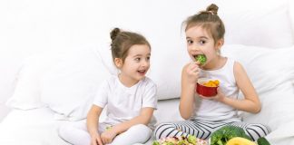 Duas crianças em meio a travesseiros e pratos de salada e frutas; imagem ilustra matéria com dicas sobre como manter a alimentação das crianças saudável.