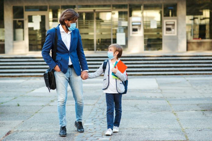 Criança de mochila e de mão dada com o pai; imagem ilustra matéria sobre retomada de aulas presenciais mundo afora.