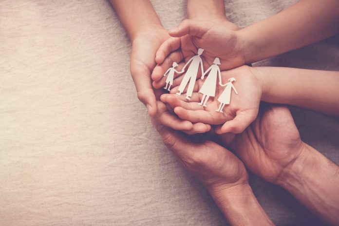 Seguro de vida: o planejamento financeiro ajuda a reduzir o sofrimento da perda; imagem mostra 4 mãos de adultos e 2 de crianças segurando bonequinhos de papel que representam uma família