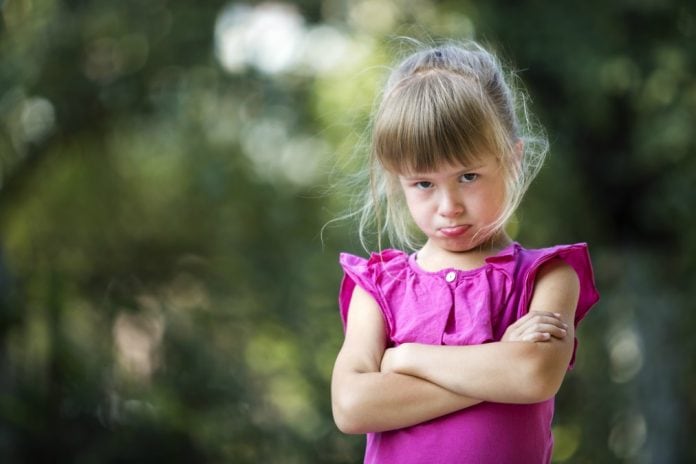 Disciplinar os filhos é essencial para que sintam-se seguros, na imagem, garota de blusa rosa e braços cruzados faz bico com a boca