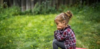 Crianças sensíveis se adaptam bem às restrições da pandemia; na imagem, garota sentada em brinquedo sob a grama apoia queixo sobre o braço e olha para a frente