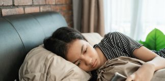 Mudanças de comportamento nas crianças chamam atenção de pediatras; na imagem, garota morena de cabelo preto está deitada na cama olhando para o celular que segura na mão
