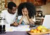 Famílias com crianças ou jovens são as mais afetadas pela pandemia; imagem mostra mulher e homem negros sentados em mesa que tem papeis e frutas
