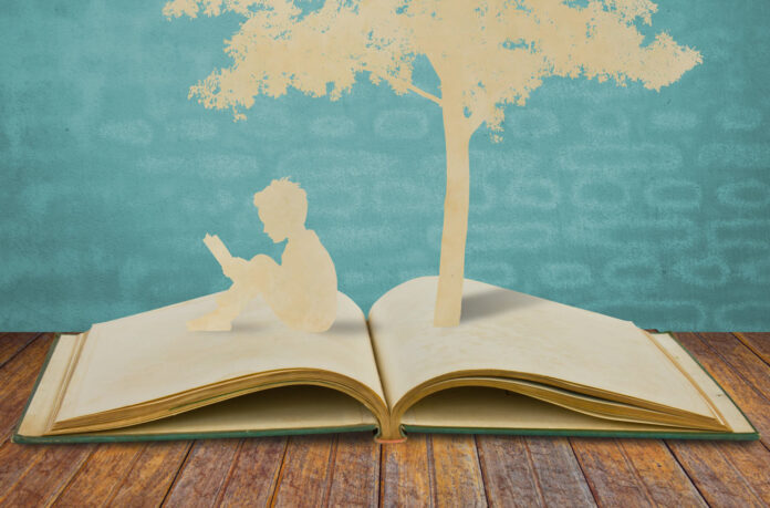 Literatura infantil e juvenil é o foco de congresso internacional; ilustração mostra livro aberta, uma criança sentada sob as páginas lendo e uma árvore ao fundo