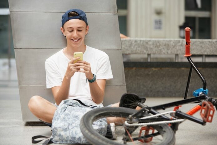Apenas 1% dos adolescentes do sexo masculino vai ao médico; imagem mostra menino jovem sentado no chão mexendo no celular com uma bicicleta do lado