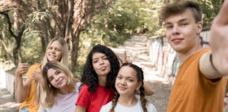 Cinco adolescentes, 4 meninas e 1 menino tiram uma selfie com uma árvore de fundo