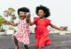 Em defesa da infância, devemos voltar para a escola, diz a pediatra Talita Rizzini; imagem mostra duas garotas negras correndo felizes, uma de vestido vermelho e a outra de vestido branco com estampas vermelhas