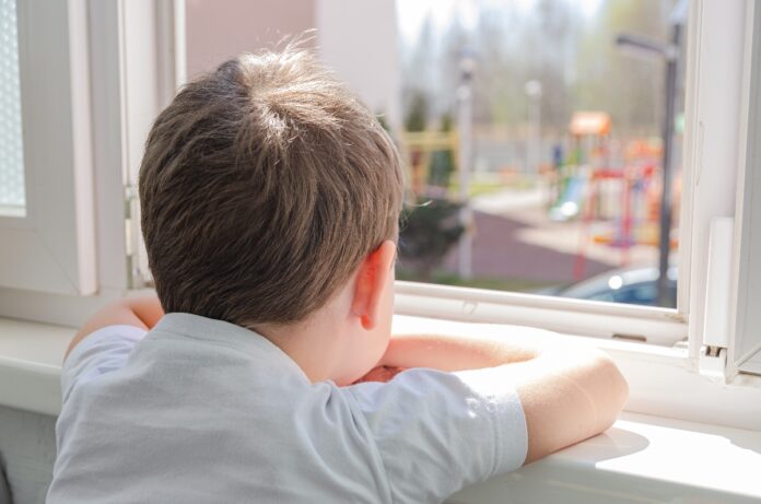 menino de costas, olhando para o lado de fora de uma janela, com o rosto apoiado nos braços cruzados