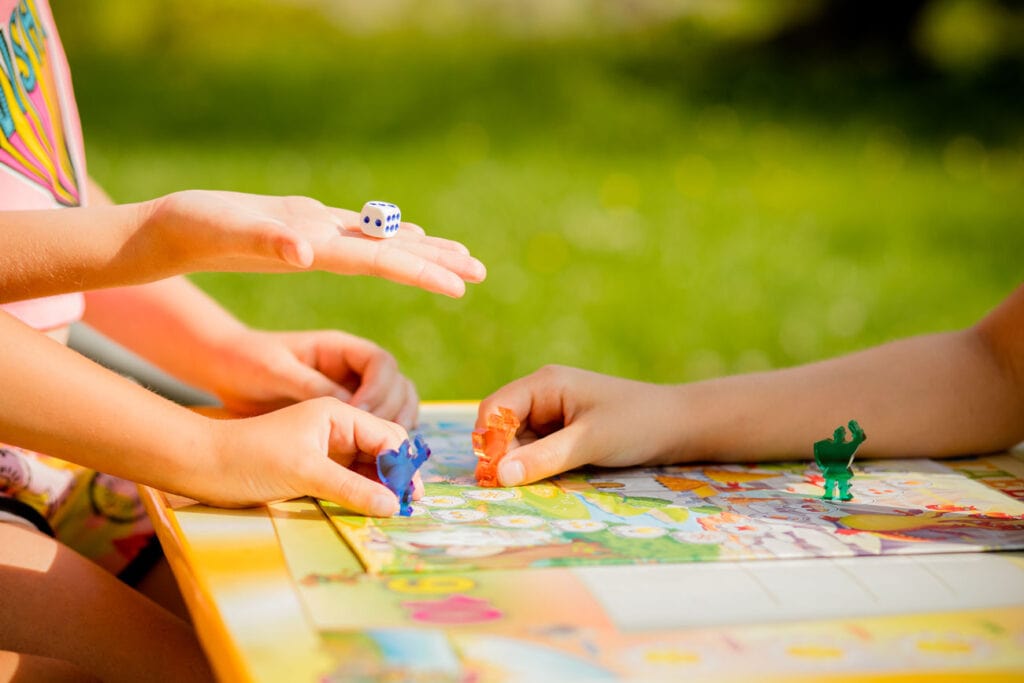 Jogos de tabuleiro para alugar – uma boa opção para divertir toda a família; imagem mostra mãos de crianças sobre tabuleiro mexendo em peças azul e vermelha