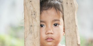Violência contra crianças é altíssima em cidades como SP e RJ; menina pequena olha através de 'grades' de madeira