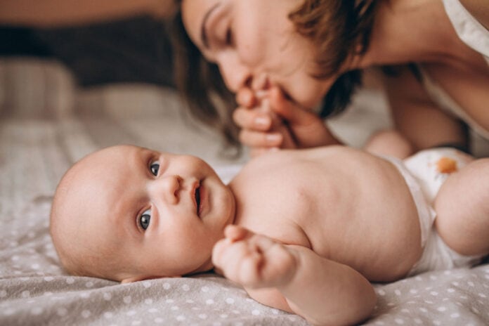 bebê de pele clara deitado na cama brincando com a mãe, medida essencial nos primeiros mil dias de vida da criança