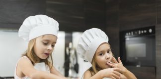 3 receitas que as crianças adoram (e usam alimentos da época); na imagem, duas meninas com chapéu de cozinheiro e avental preparam salada
