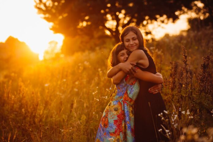 O abraço: 'Escolha quem você quer abraçar, porque abraço faz falta'; imagem mostra mãe e filha se abraçando em meio ao campo com o por do sol ao fundo