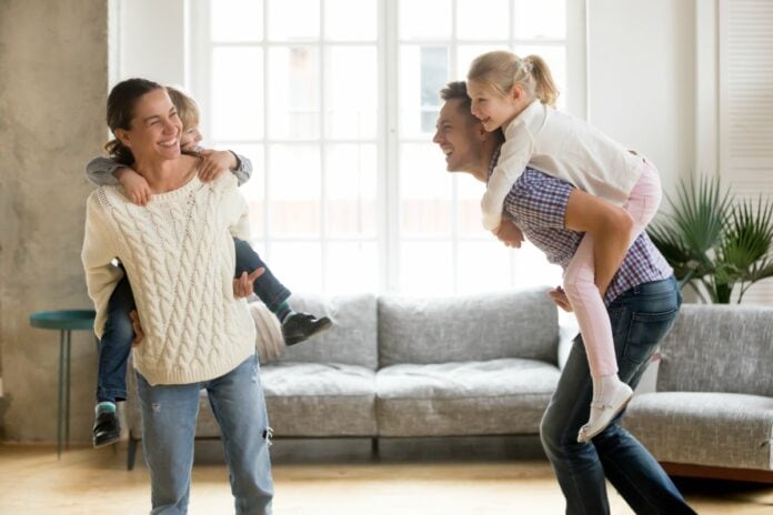 Pais felizes ajudam a formar filhos igualmente felizes; imagem mostra mãe e pai com os filhos na corcunda na sala de casa