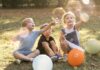Criança deve ser, antes de tudo, criança; imagem mostra três crianças sentadas na grama brincando com bexigas e bolhas de sabão