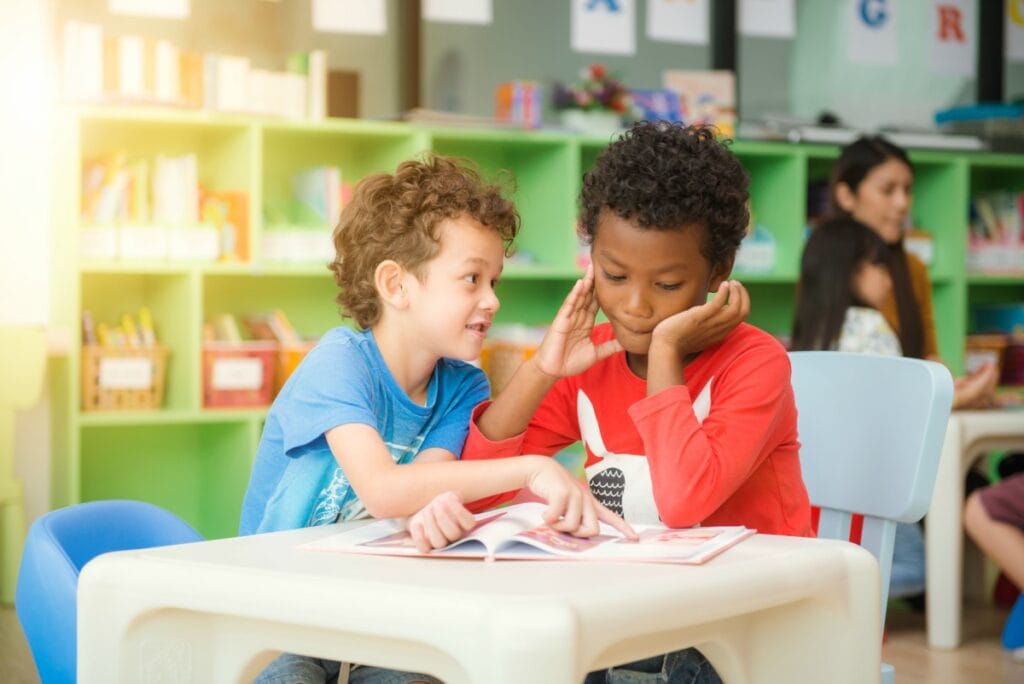 O que observar na hora da escolha da escola de seu filho; imagem mostra dois meninos, um moreno e outro ruivo folheando livro sobre carteira escolar