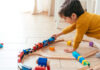 Menino brincando sozinho de trenzinho de madeira no chão, umas das atividades que pode ser feita para incentivar a criança a brincar sozinha