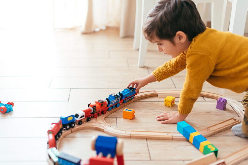 Menino brincando sozinho de trenzinho de madeira no chão, umas das atividades que pode ser feita para incentivar a criança a brincar sozinha