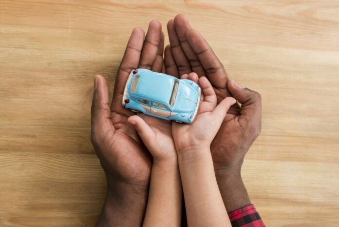 Brasil tem 30 mil crianças acolhidas e 5 mil aptas para adoção; imagem mostra mãos de adulto envolvendo mãos de uma criança que segura um carrinho azul claro