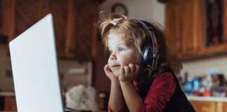 Coleta online de dados de crianças para publicidade infantil é preocupante; imagem mostra criança com fone de ouvido sentada e olhando para tela de desktop sobre mesa