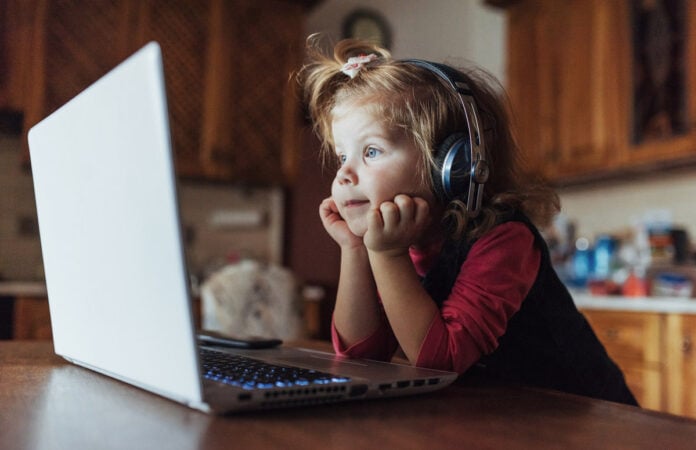 Coleta online de dados de crianças para publicidade infantil é preocupante; imagem mostra criança com fone de ouvido sentada e olhando para tela de desktop sobre mesa